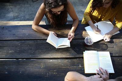 Three people sat at a picnic table reading and writing